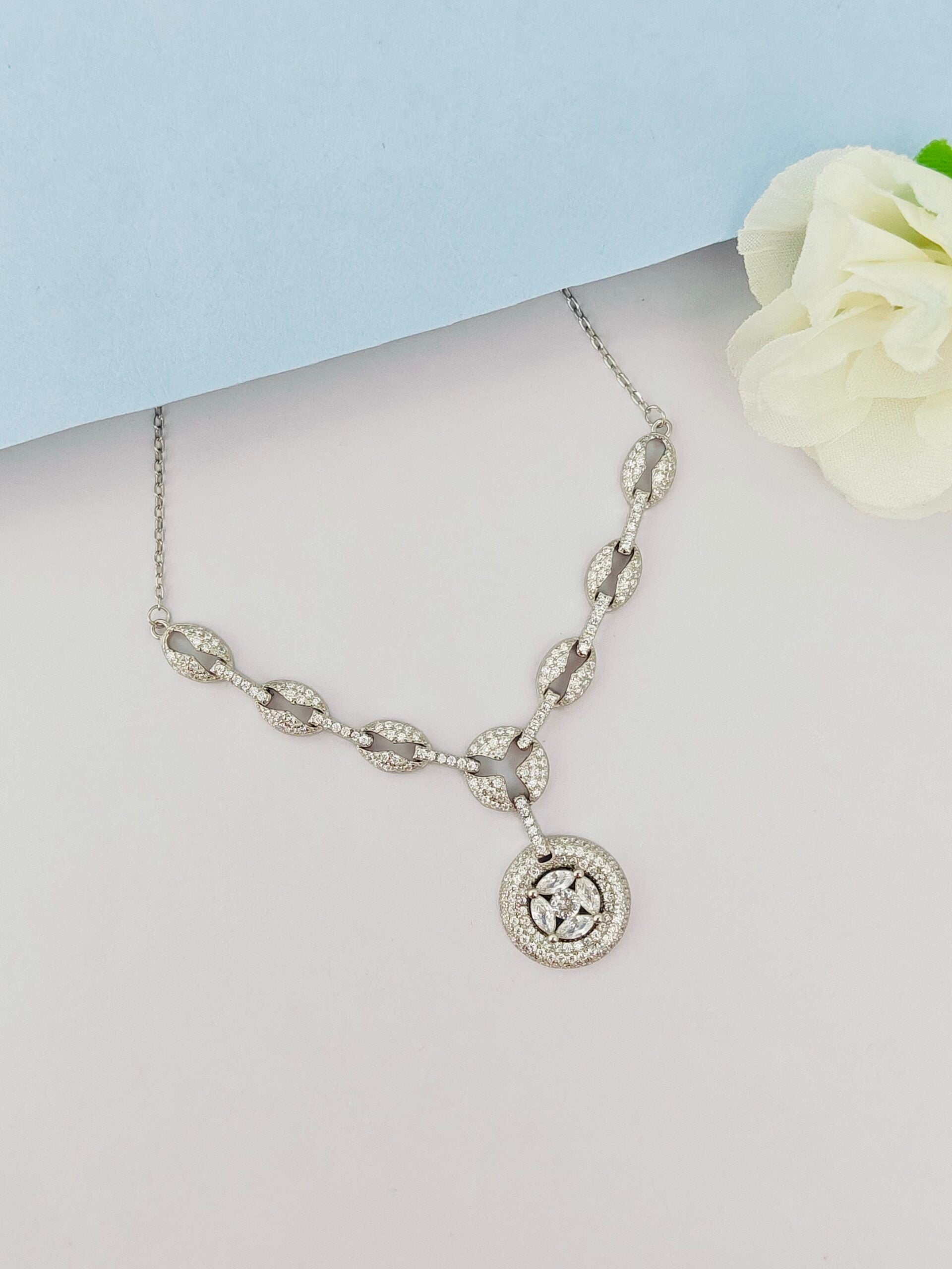 Silver necklace with a circular pendant on a light gray surface with a white flower.
